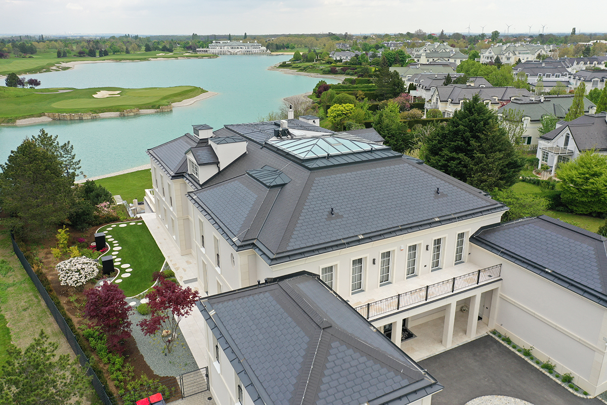  Luxusní vila s tmavou střechou, střešním světlíkem a upravenou zahradou s výhledem na jezero a golfové hřiště.