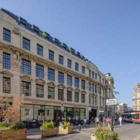 Historická budova v Oxfordu s renovovanou fasádou a velkými industriálními okny. V přízemí se nachází obchody a hotel The Store.