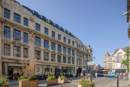 Historická budova v Oxfordu s renovovanou fasádou a velkými industriálními okny. V přízemí se nachází obchody a hotel The Store.